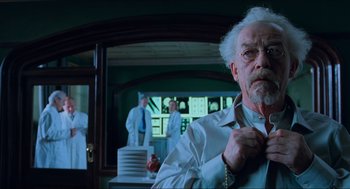 Movie still from “Hellboy” (2004), directed by Guillermo del Toro – An older man in a white lab coat is adjusting his tie in front of a mirror; Medium shot, Low angle