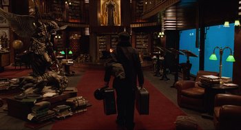 Movie still from “Hellboy” (2004), directed by Guillermo del Toro – A man walking through a library holding two suitcases; Wide shot, Low angle
