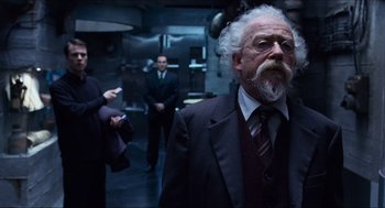 Movie still from “Hellboy” (2004), directed by Guillermo del Toro – An older man in a suit and tie in front of two other people; Medium shot, Low angle