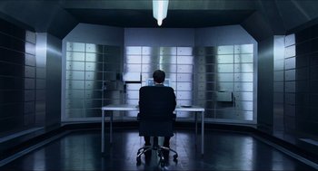 Movie still from “Hellboy” (2004), directed by Guillermo del Toro – A man sitting at a desk in front of a row of mailboxes; Wide shot, High angle