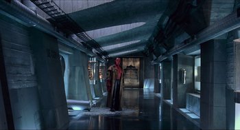 Movie still from “Hellboy” (2004), directed by Guillermo del Toro – A man dressed in a red outfit standing in an empty room; Wide shot, High angle