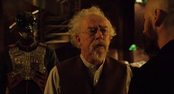 Movie still from “Hellboy” (2004), directed by Guillermo del Toro – An older man with a white beard wearing glasses and a brown vest; Medium shot, Low angle