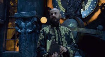 Movie still from “Hellboy” (2004), directed by Guillermo del Toro – A man in a black and gold jacket holding a book; Medium shot, Low angle