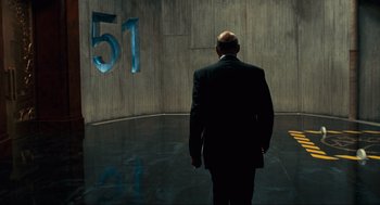 Movie still from “Hellboy II: The Golden Army” (2008), directed by Guillermo del Toro – A man in a black suit is standing in front of a wall; Wide shot, Low angle