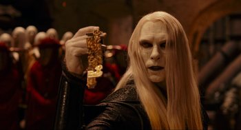 Movie still from “Hellboy II: The Golden Army” (2008), directed by Guillermo del Toro – A person with long white hair holding up a piece of food; Close Up shot, Over the shoulder angle