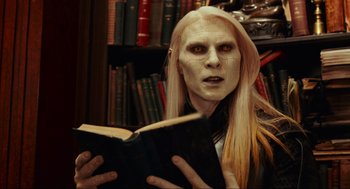 Movie still from “Hellboy II: The Golden Army” (2008), directed by Guillermo del Toro – A man with long blonde hair is reading a book in a library; Close Up shot, High angle