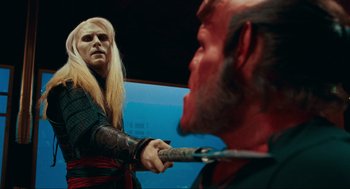 Movie still from “Hellboy II: The Golden Army” (2008), directed by Guillermo del Toro – A man with long blonde hair holding a pair of shears in front of another man with long hair; Medium shot, Over the shoulder angle