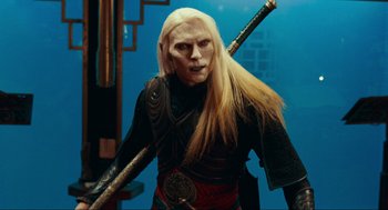 Movie still from “Hellboy II: The Golden Army” (2008), directed by Guillermo del Toro – A man with long blonde hair and a white face holding two swords; Medium shot, Over the shoulder angle