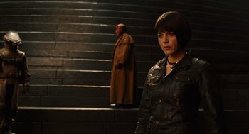Movie still from “Hellboy II: The Golden Army” (2008), directed by Guillermo del Toro – A woman standing in front of a staircase with a man in the background; Medium shot, Over the shoulder angle