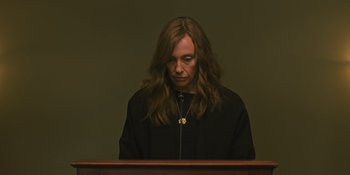 Movie still from “Hereditary” (2018), directed by Ari Aster – A person with long brown hair is sitting at a table; Medium shot, Low angle