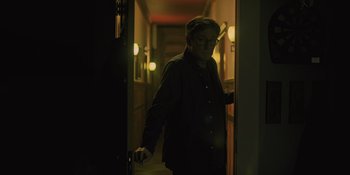 Movie still from “Hereditary” (2018), directed by Ari Aster – A man standing in a dark room holding a door; Medium shot, Low angle