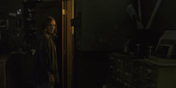Movie still from “Hereditary” (2018), directed by Ari Aster – A woman standing in a dark room next to an open door; Medium shot, Over the shoulder angle