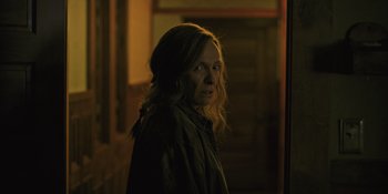 Movie still from “Hereditary” (2018), directed by Ari Aster – A woman standing in a room with a dark background; Close Up shot, Over the shoulder angle