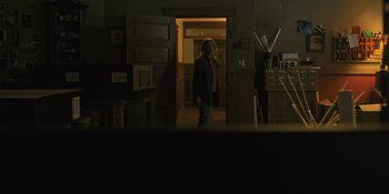 Movie still from “Hereditary” (2018), directed by Ari Aster – A woman standing in a dark room in front of an open door; Wide shot, Low angle