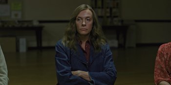 Movie still from “Hereditary” (2018), directed by Ari Aster – A woman with long brown hair wearing a blue jacket; Medium shot, High angle