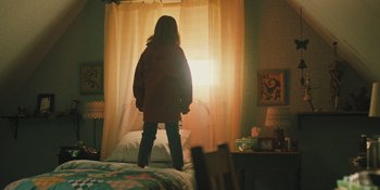 Movie still from “Hereditary” (2018), directed by Ari Aster – A woman standing in front of a window in a room; Medium shot, Low angle