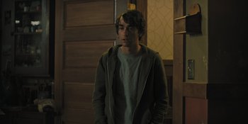 Movie still from “Hereditary” (2018), directed by Ari Aster – A man standing in front of a wooden door; Medium shot, Over the shoulder angle