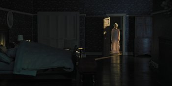 Movie still from “Hereditary” (2018), directed by Ari Aster – A woman standing in a doorway in a dark room; Wide shot, High angle