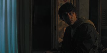 Movie still from “Hereditary” (2018), directed by Ari Aster – A man in a dark room looking at the camera; Medium shot, Over the shoulder angle