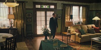 Movie still from “Hereditary” (2018), directed by Ari Aster – A man in a suit standing next to a table; Wide shot, Over the shoulder angle
