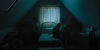 Movie still from “Hereditary” (2018), directed by Ari Aster – A person sitting on a bed in a room; Wide shot, High angle