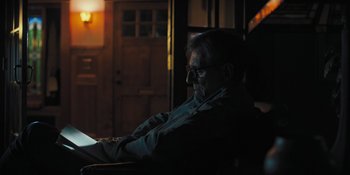 Movie still from “Hereditary” (2018), directed by Ari Aster – A man sitting in the dark looking at a book; Medium shot, High angle
