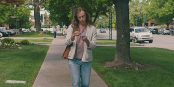 Movie still from “Hereditary” (2018), directed by Ari Aster – A woman walking down a sidewalk while looking at her cell phone; Medium shot, Over the shoulder angle
