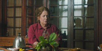 Movie still from “Hereditary” (2018), directed by Ari Aster – An older woman sitting at a table in front of a plant; Close Up shot, Over the shoulder angle