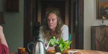 Movie still from “Hereditary” (2018), directed by Ari Aster – A woman sitting at a table with a tea pot; Medium shot, High angle