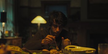 Movie still from “Hereditary” (2018), directed by Ari Aster – A man sitting at a dinner table eating food; Medium shot, High angle