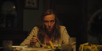 Movie still from “Hereditary” (2018), directed by Ari Aster – A woman sitting at a table with a plate in front of her; Medium shot, Over the shoulder angle