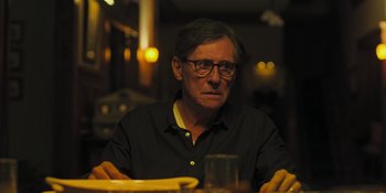 Movie still from “Hereditary” (2018), directed by Ari Aster – A man sitting at a table with a glass of wine; Close Up shot, Over the shoulder angle