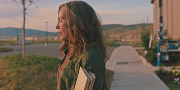 Movie still from “Hereditary” (2018), directed by Ari Aster – A woman walking down a sidewalk holding a book; Medium shot, Over the shoulder angle