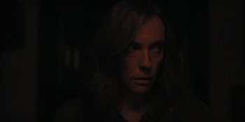 Movie still from “Hereditary” (2018), directed by Ari Aster – A woman with long brown hair is in the dark; Close Up shot, Over the shoulder angle