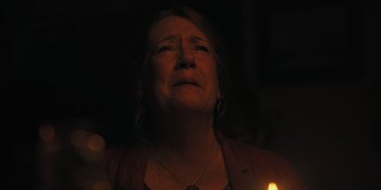 Movie still from “Hereditary” (2018), directed by Ari Aster – An older woman with her eyes closed with a candle in the dark; Close Up shot, Over the shoulder angle