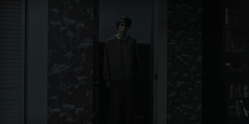 Movie still from “Hereditary” (2018), directed by Ari Aster – A man standing in a dark room in front of a door; Wide shot, High angle