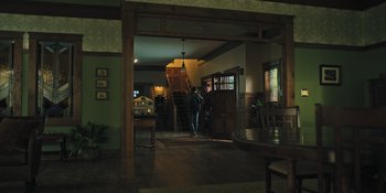 Movie still from “Hereditary” (2018), directed by Ari Aster – A man standing in a room next to a staircase; Wide shot, Low angle