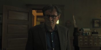 Movie still from “Hereditary” (2018), directed by Ari Aster – A man wearing a suit and glasses in a room; Close Up shot, Low angle