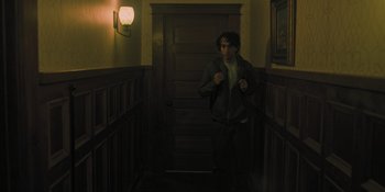 Movie still from “Hereditary” (2018), directed by Ari Aster – A man walking down the stairs in a dark room; Medium shot, High angle