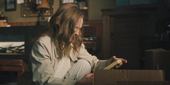 Movie still from “Hereditary” (2018), directed by Ari Aster – A woman sitting on the floor looking at an open box; Medium shot, High angle