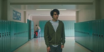 Movie still from “Hereditary” (2018), directed by Ari Aster – A young man standing in a school hallway with his hands in his pockets; Medium shot, Low angle