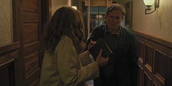 Movie still from “Hereditary” (2018), directed by Ari Aster – A man and a woman are standing in front of each other holding a notebook; Medium shot, Over the shoulder angle