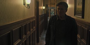 Movie still from “Hereditary” (2018), directed by Ari Aster – An older man standing in a dark hallway; Medium shot, Over the shoulder angle