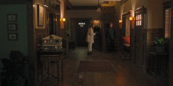 Movie still from “Hereditary” (2018), directed by Ari Aster – Two people standing in a room with a table and chairs in front of them; Wide shot, High angle