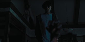 Movie still from “Hereditary” (2018), directed by Ari Aster – A man standing in a dark room holding a hand up; Medium shot, Over the shoulder angle