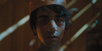 Movie still from “Hereditary” (2018), directed by Ari Aster – A young man wearing a paper hat and a nose; Close Up shot, High angle