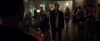 Movie still from “Hitch” (2005), directed by Andy Tennant – A man holding a pool stick in a room with people; Wide shot, Over the shoulder angle