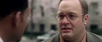Movie still from “Hitch” (2005), directed by Andy Tennant – A person wearing glasses with buildings in the background; Close Up shot, Over the shoulder angle