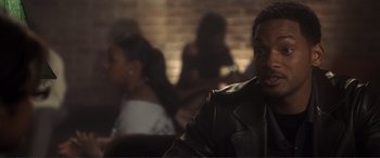 Movie still from “Hitch” (2005), directed by Andy Tennant – A man in a leather jacket sitting in front of a brick wall; Close Up shot, Over the shoulder angle