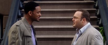 Movie still from “Hitch” (2005), directed by Andy Tennant – Two men standing next to each other in front of a set of stairs; Medium shot, Over the shoulder angle